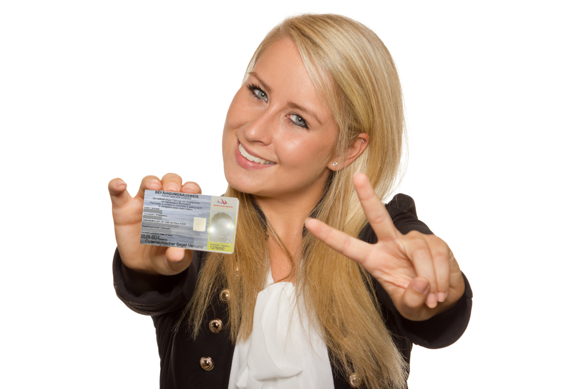 Blonde Dame zeigt mit einer Hand das Victory-Symbol und hält einen Bootsführerschein in der anderen Hand